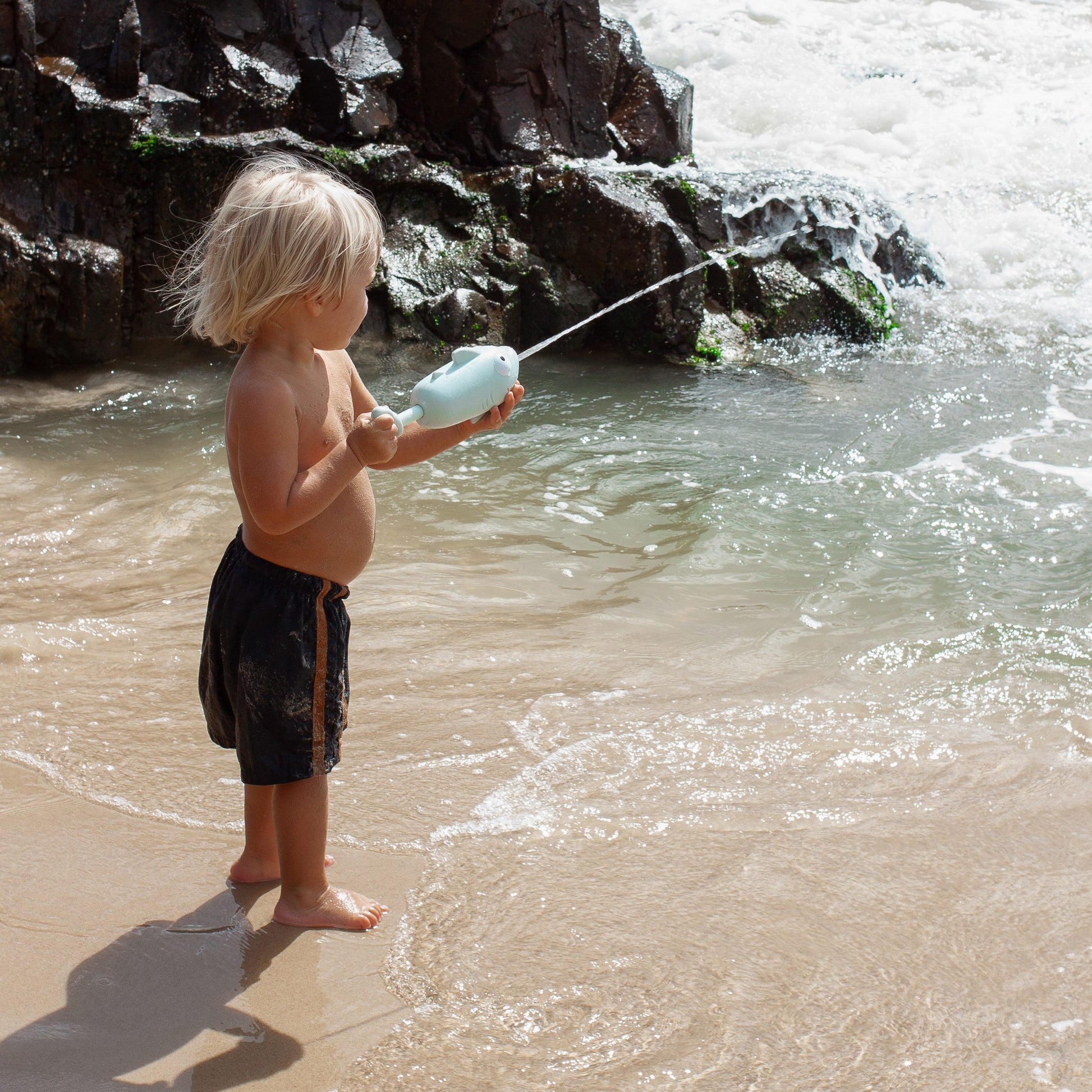 Dziecko bawiące się pistoletem wodnym rekin dla dzieci na plaży przy morzu