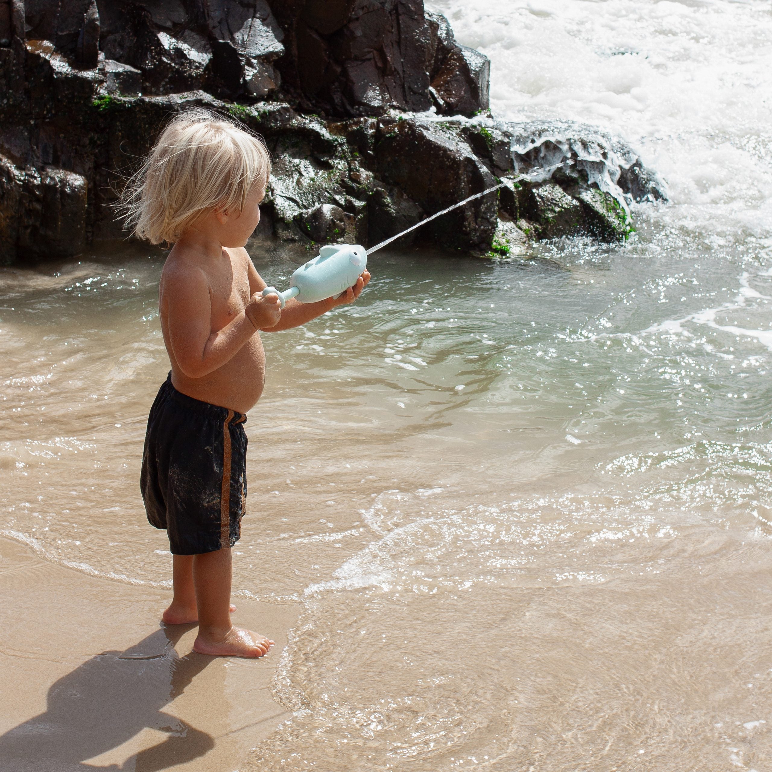 Dziecko bawiące się pistoletem wodnym rekin dla dzieci na plaży przy morzu