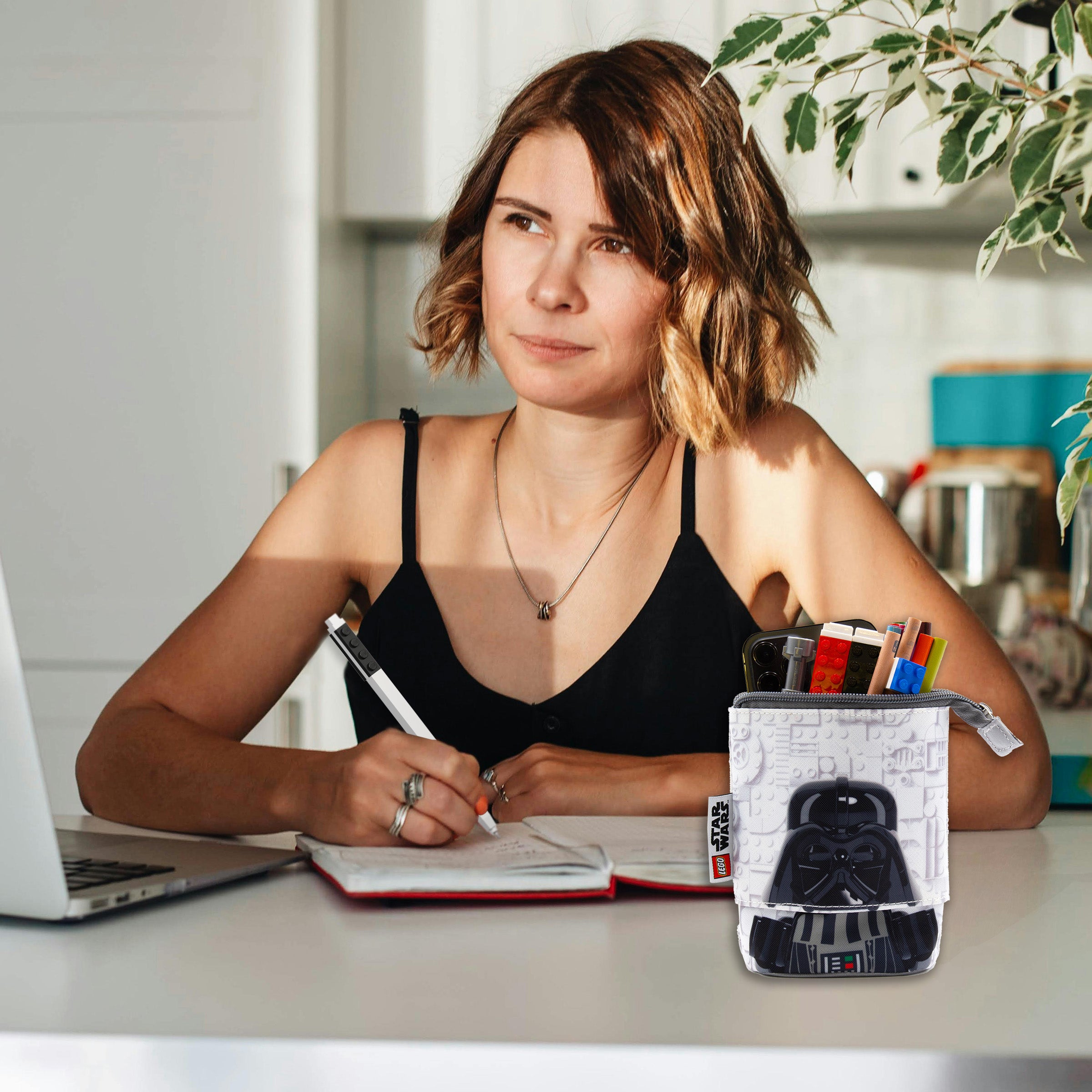 Piórnik LEGO Star Wars z motywem Dartha Vadera na biurku obok kobiety piszącej notatki