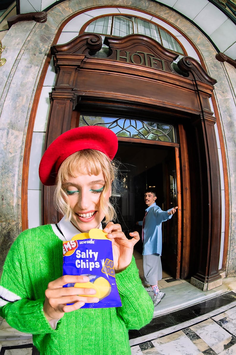 Skarpetki chipsy prezent EMS na opakowaniu przypominającym paczkę chipsów trzymane przez kobietę w czerwonym berecie i zielonym swetrze