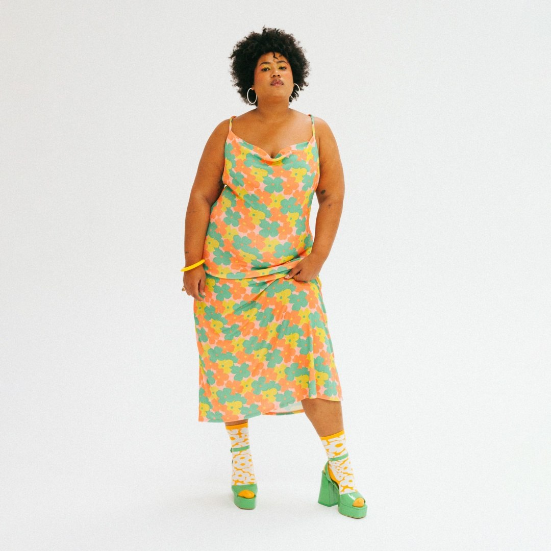 Kobieta w kolorowej sukience i skarpetkach ems flower power w kwiatowy wzór z zielonymi sandałami