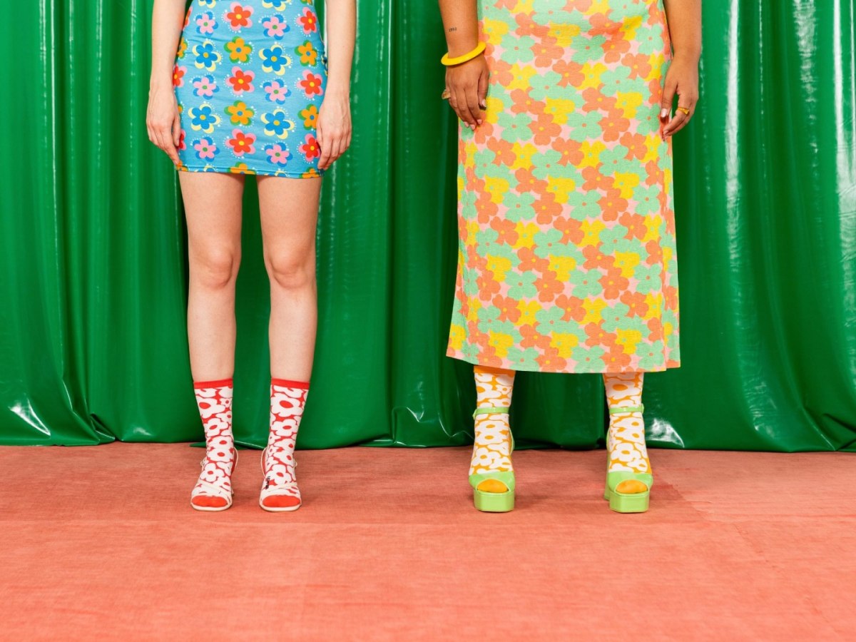 Dwie osoby noszące skarpetki ems flower power z kolorowym kwiatowym wzorem na tle zielonej zasłony