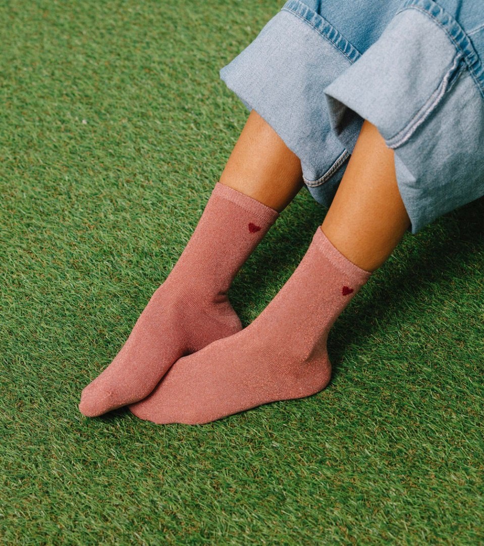 Różowe skarpetki prezentowe w kształcie serca na stopach osoby siedzącej na zielonej trawie