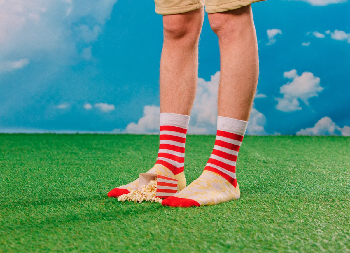 Męskie skarpetki popcorn w paski czerwono-białe i kremowe na trawie z rozsypanym popcornem