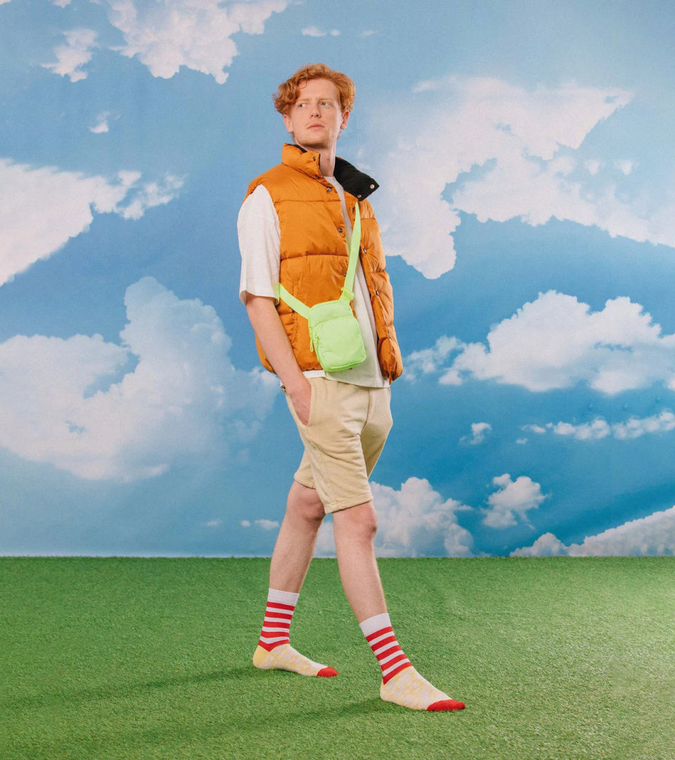 Mężczyzna w pomarańczowej kamizelce i skarpetkach popcorn w czerwono-białe paski na zielonej trawie