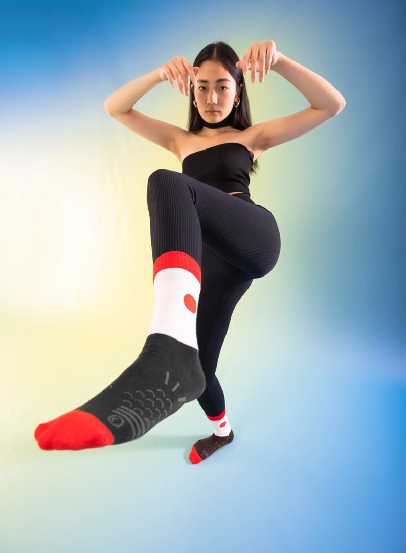 Kobieta pokazująca czarne i czerwone elektryczne skarpetki EMS na tle gradientu