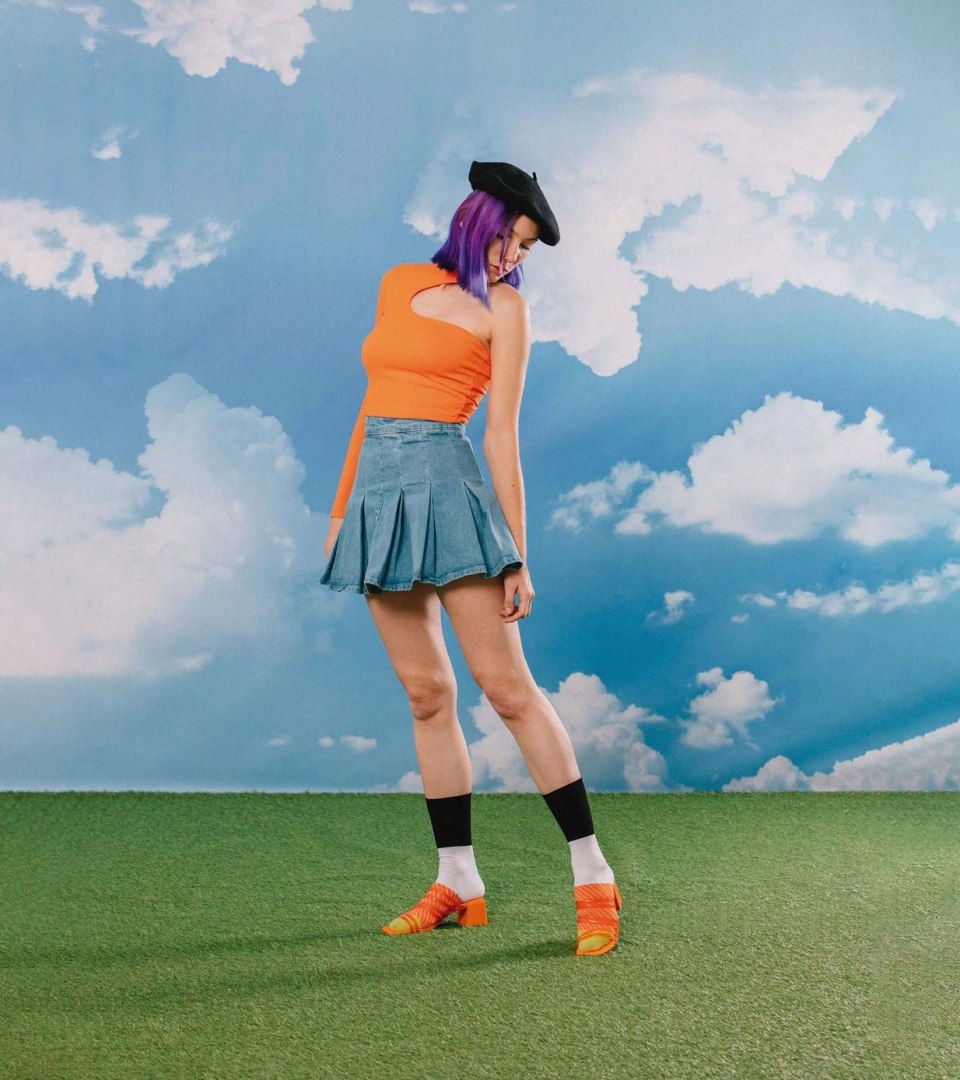 Modelka w skarpetkach sushi box WABOBA AB, pomarańczowym topie i spódnicy na tle nieba z chmurami