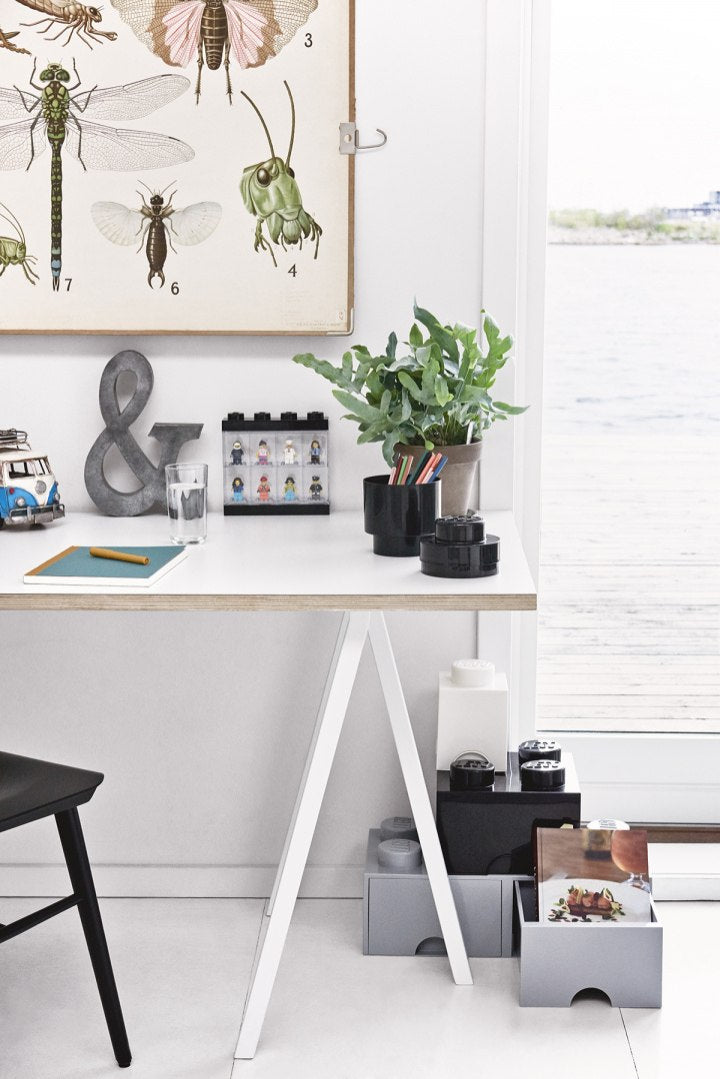 Organizator szuflada LEGO Brick 4 czarna umieszczona pod białym biurkiem w jasnym pokoju z rośliną na blacie