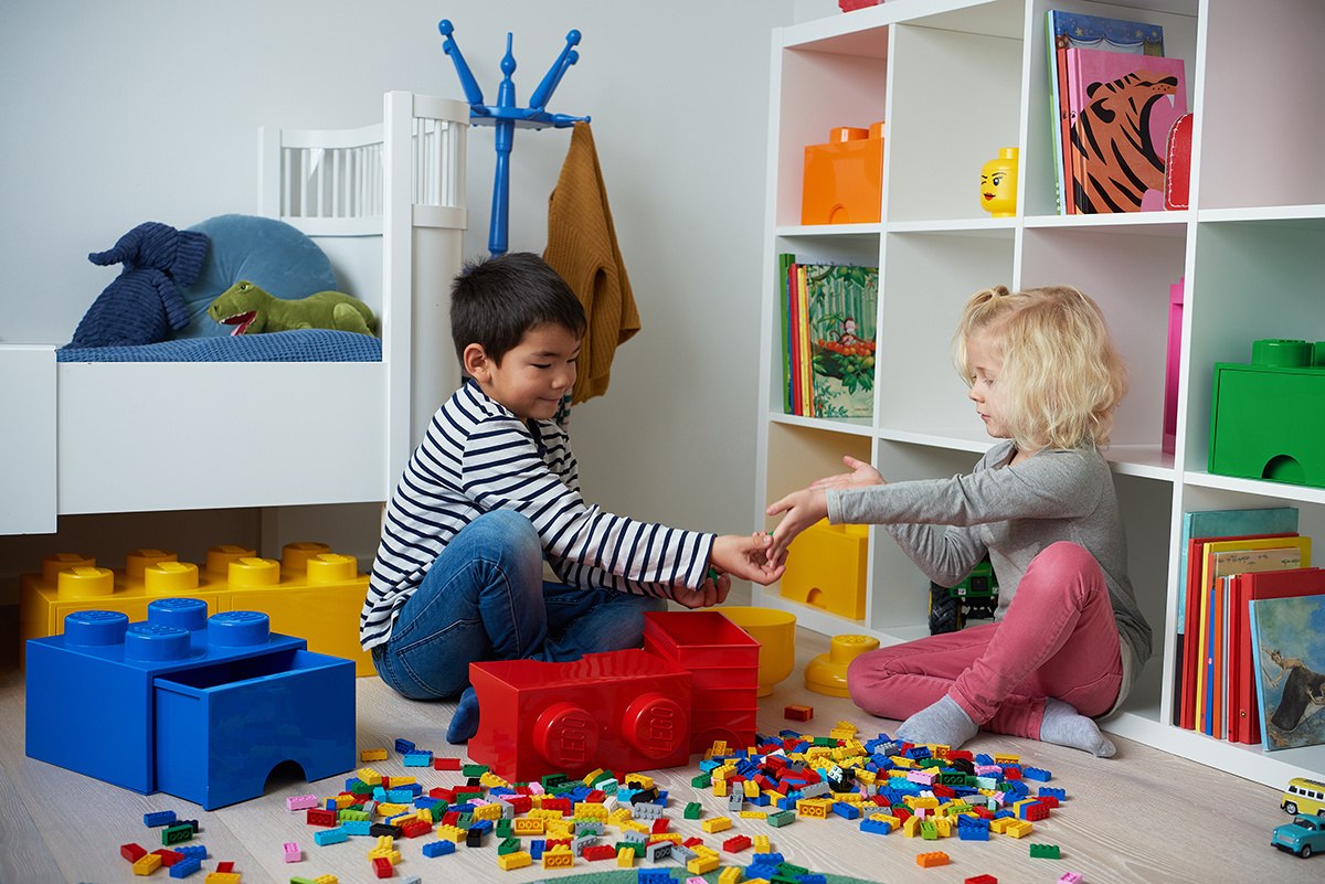 Dzieci bawiące się przy szufladzie LEGO na zabawki w kształcie klocka na podłodze pokoju dziecięcego