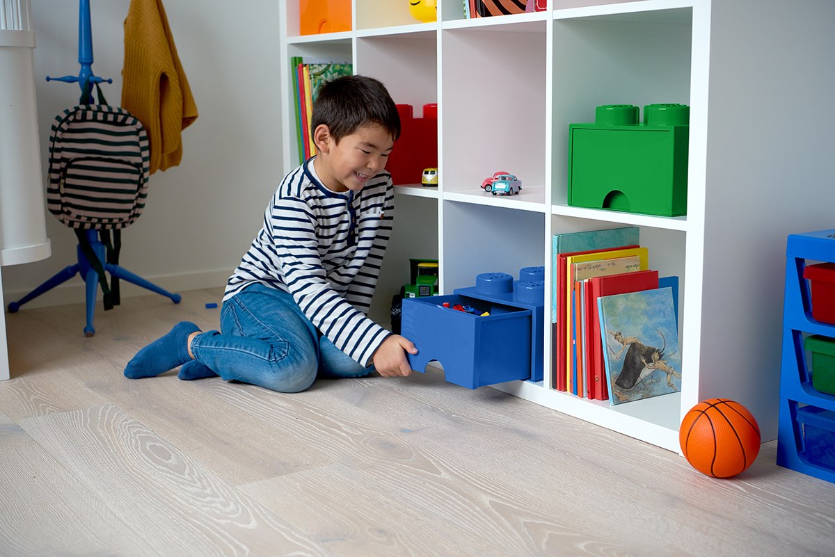 Chłopiec wyciąga niebieską szufladę LEGO na zabawki z białej półki w pokoju dziecięcym
