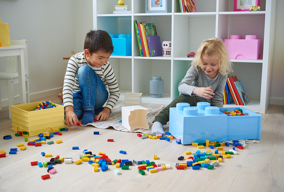 Dzieci bawiące się na podłodze z klockami LEGO i jasnoniebieską szufladą LEGO Brick 4 do przechowywania