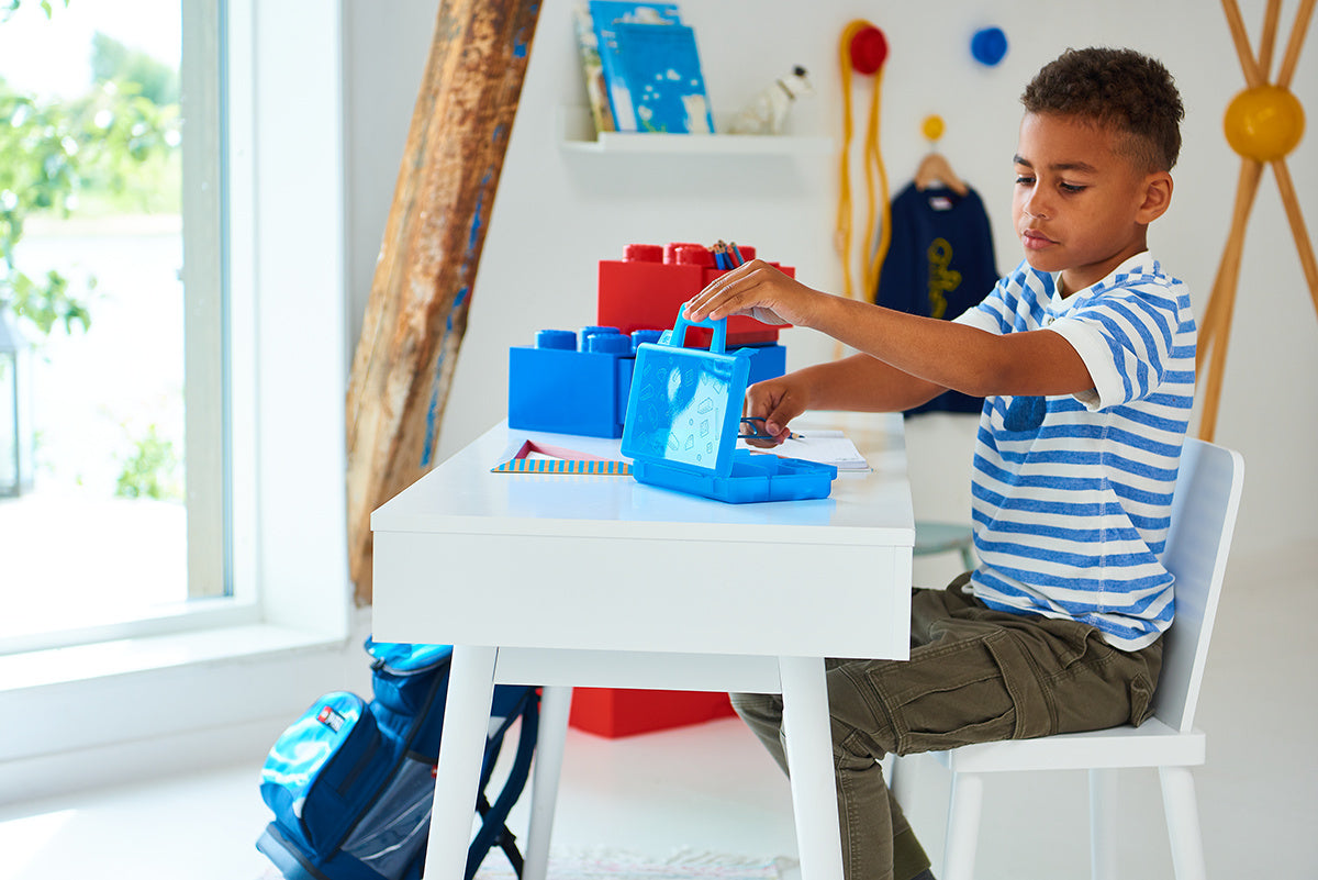 Chłopiec bawiący się szufladką LEGO na biurko przy białym stole w jasnym pokoju