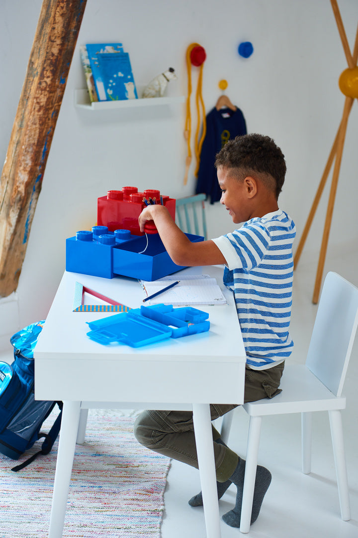 Dziecko bawiące się na biurku z niebieską szufladką LEGO na biurko do przechowywania klocków