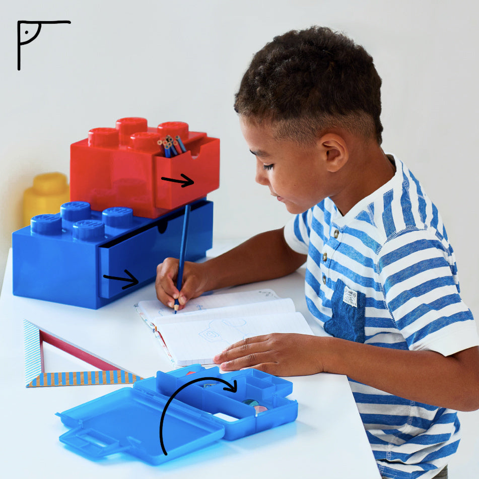 Szufladka LEGO na biurko w kolorach czerwonym i niebieskim z przegródkami na przybory szkolne obok dziecka piszącego w zeszycie