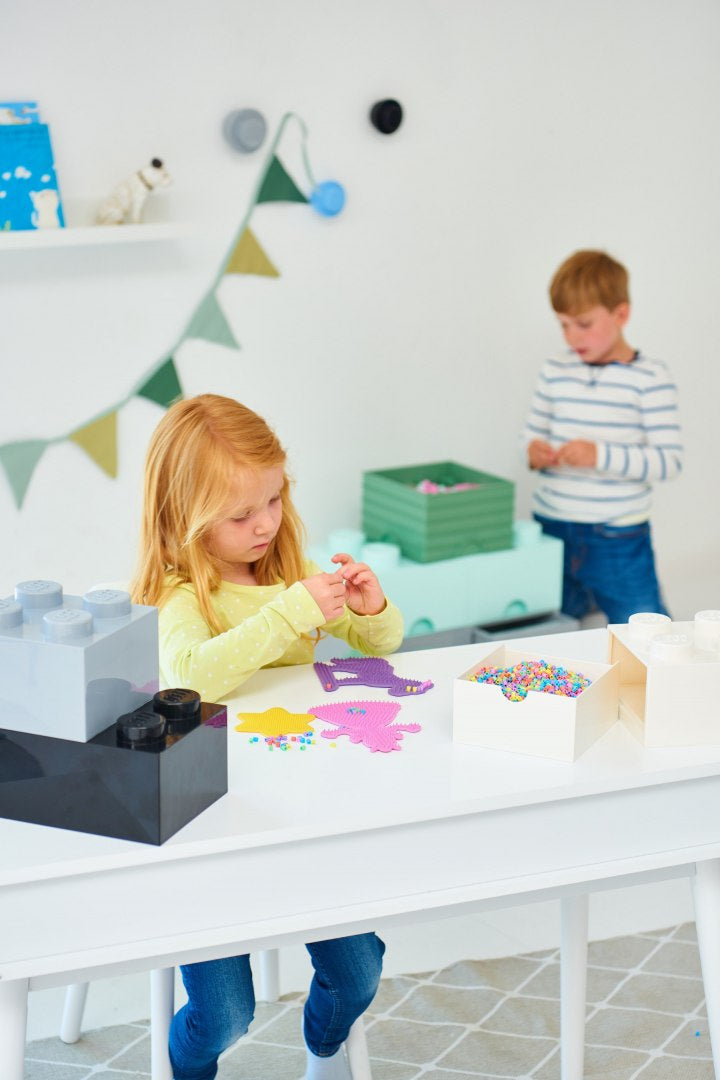 Dzieci bawiące się przy białym stole z szufladką LEGO na biurko w jasnym pokoju zabaw