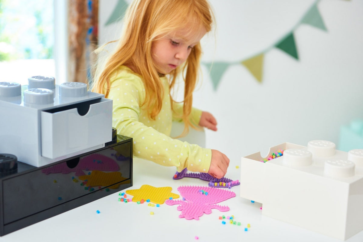Szufladka LEGO na biurko w kształcie klocka, z dzieckiem bawiącym się koralikami przy stole
