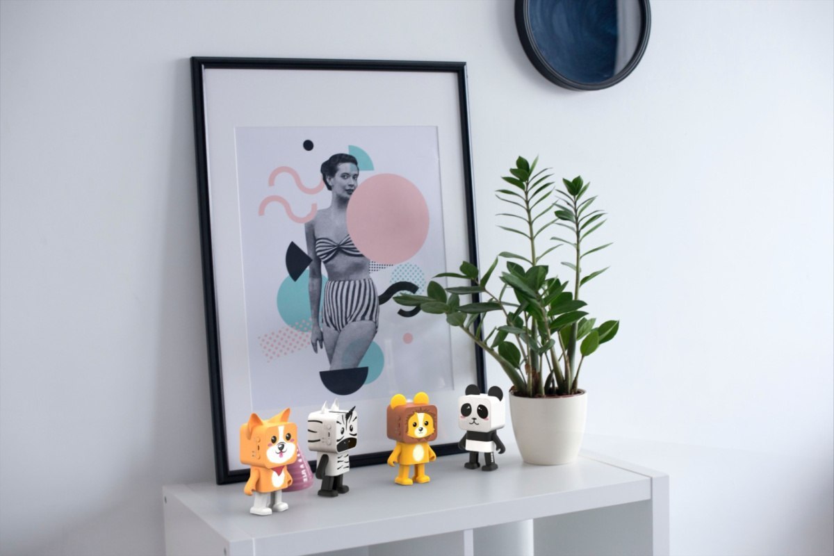 Tańczący głośnik bezprzewodowy panda i inne kolorowe figurki stojące na białej szafce obok doniczki z rośliną