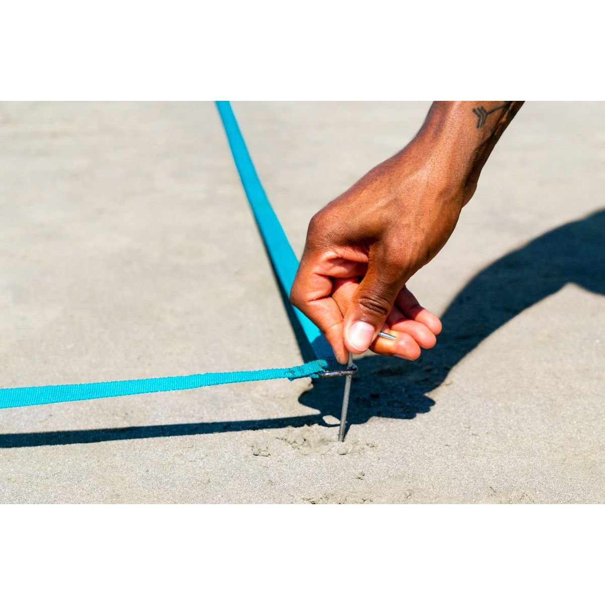 Ręka mocująca niebieską taśmę do ziemi podczas terenowej gry zręcznościowej dla dzieci