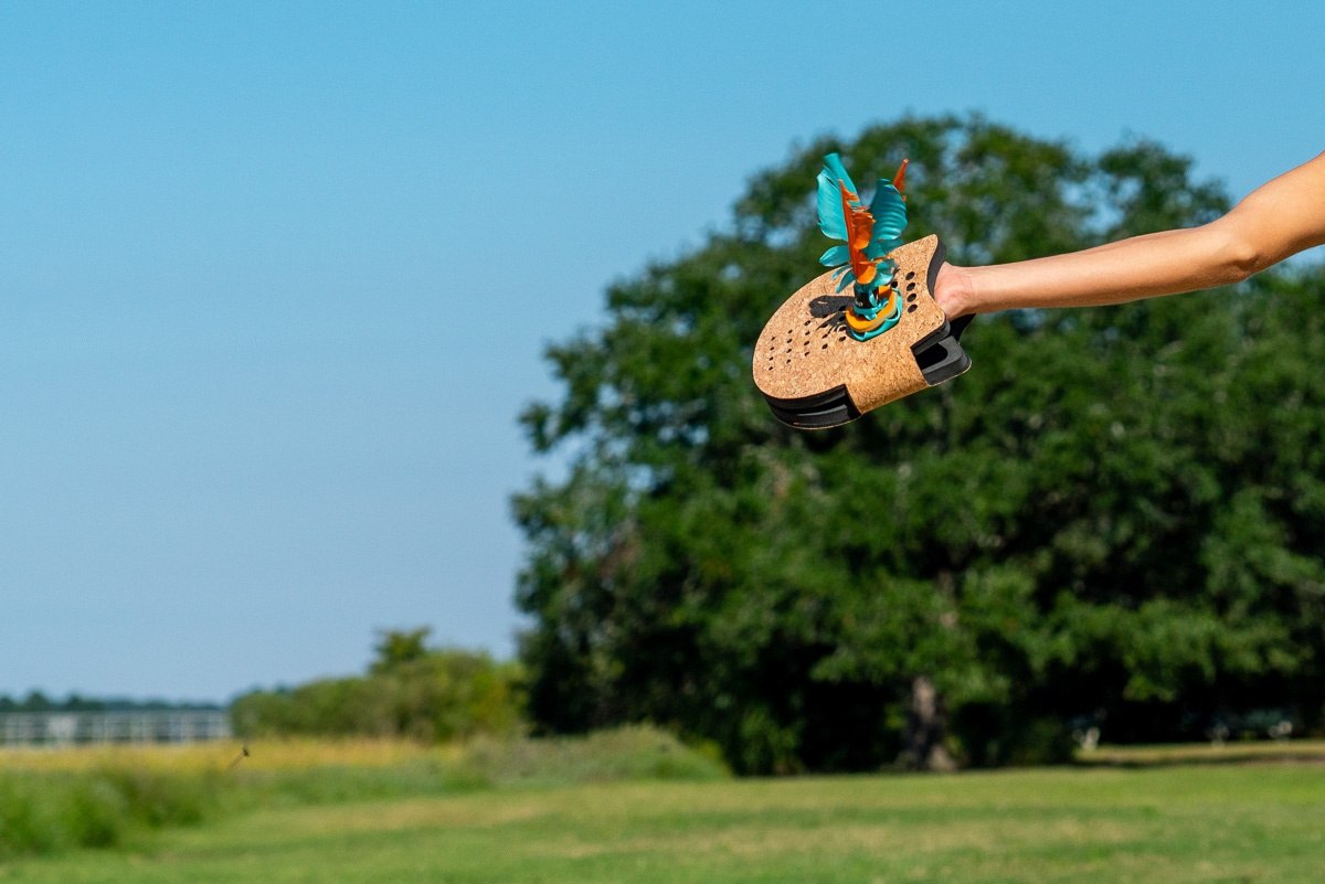 Ręka trzymająca terenową grę zręcznościową Waboba Voli na tle zielonego pola i nieba