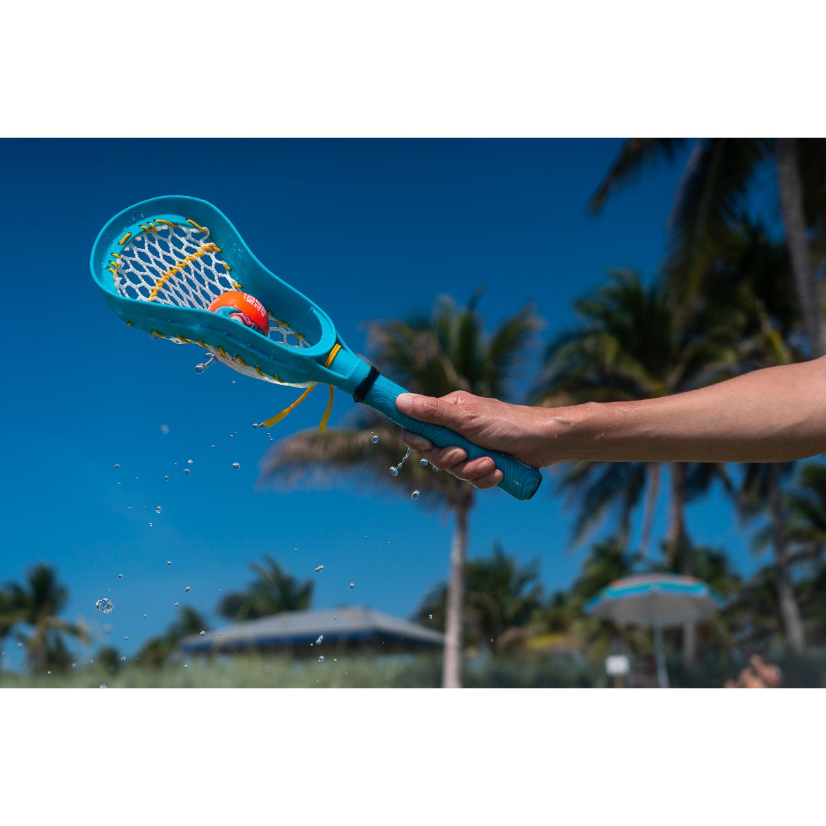 Yamann zestaw do lacrosse dla dzieci niebieska pałka z piłką trzymana na tle nieba i palm