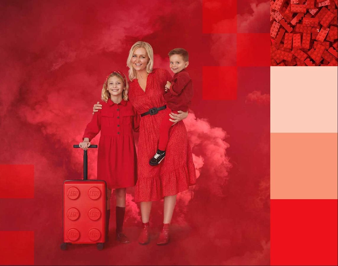 Czerwona walizka LEGO Signature czerwona na kółkach obok kobiety i dzieci w czerwonych ubraniach