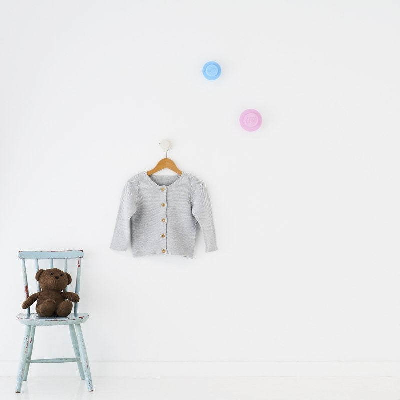 Wieszaki LEGO jasnoniebieski różowy biały na ścianie z szarym sweterkiem i niebieskim krzesełkiem z misiem