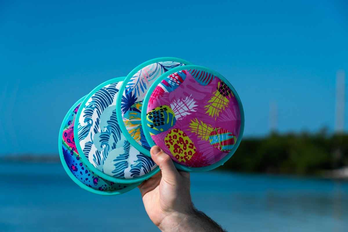 Kolorowe frisbee wodne dla dzieci o tropikalnych wzorach trzymane na tle niebieskiego nieba i wody