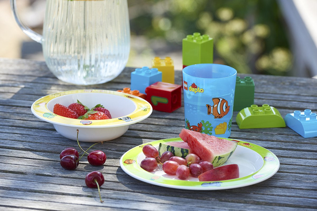 Zestaw naczyń LEGO Duplo z kolorowymi talerzami, kubkiem i pojemnikami na stole ogrodowym