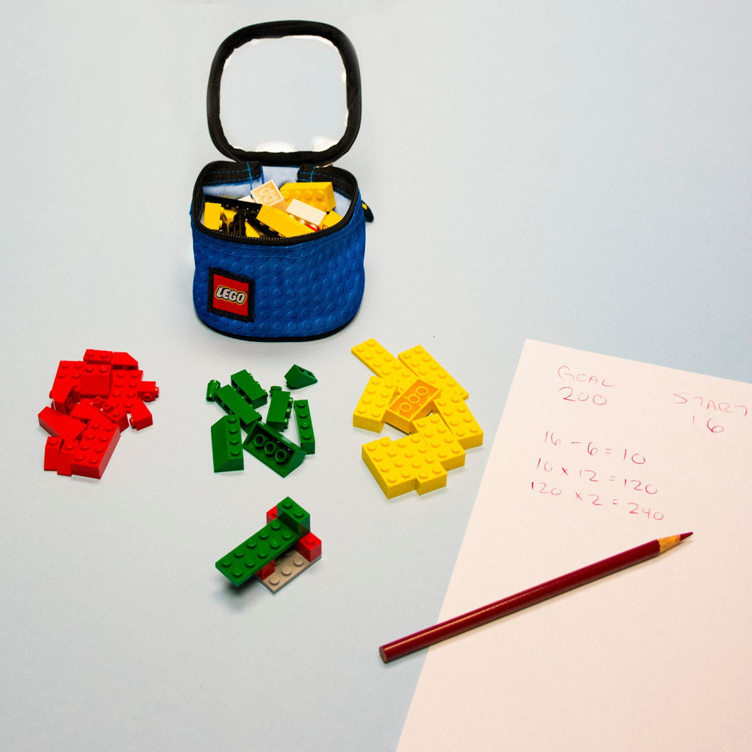 Niebieski organizer LEGO na klocki z segregowanymi czerwonymi, zielonymi i żółtymi klockami LEGO na stole obok kartki z notatkami