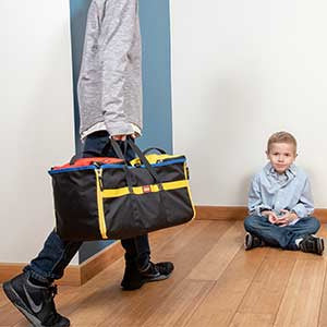 Czarna torba podróżna z uchwytami i żółtymi akcentami na drewnianej podłodze obok siedzącego chłopca zestaw pojemników LEGO z matą