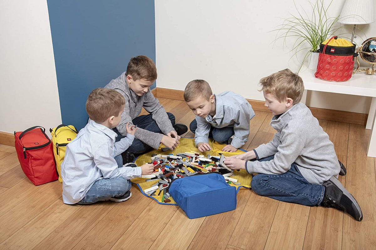 Cztery chłopcy bawią się zestawem pojemników LEGO z matą na drewnianej podłodze w pokoju