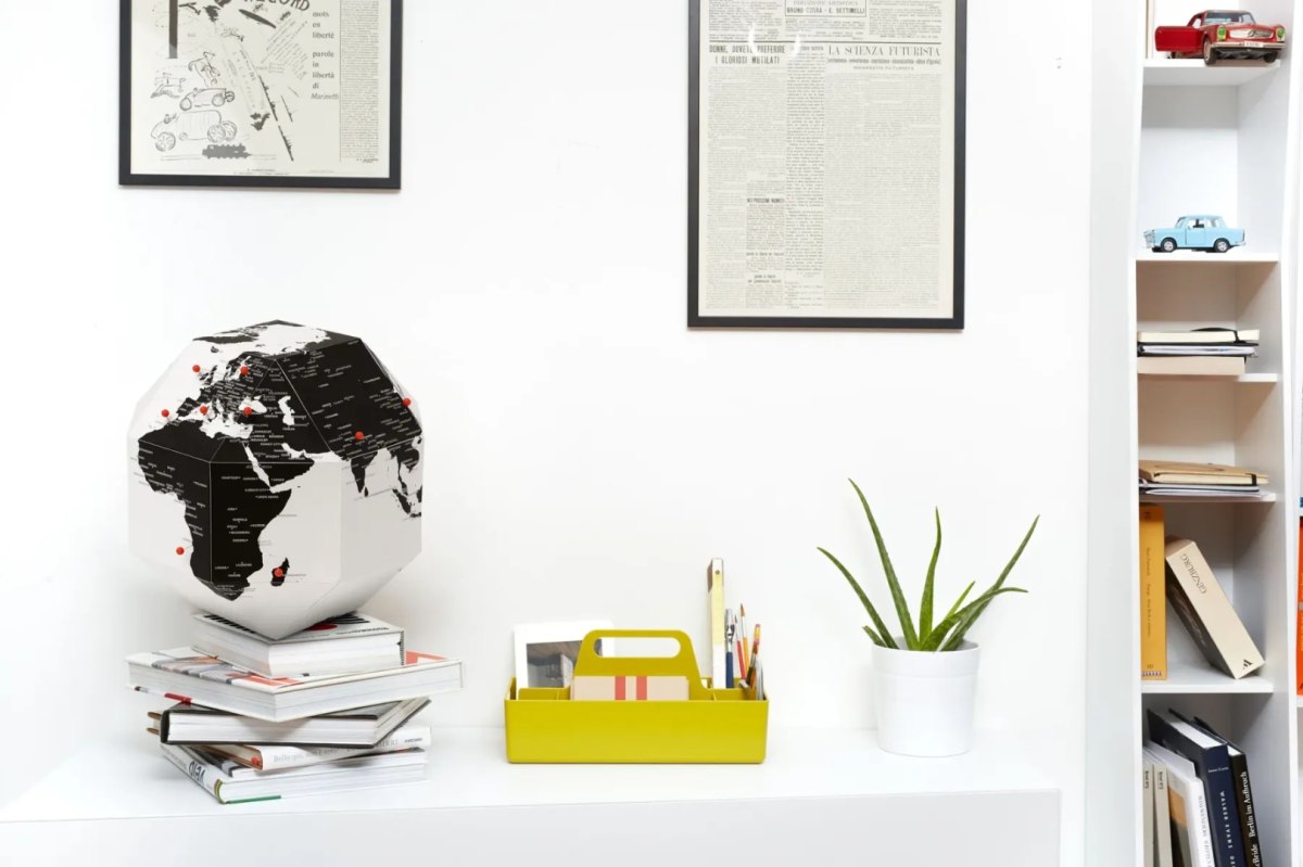 Globus z pinezkami do oznaczania krajów na białym biurku z rośliną i książkami