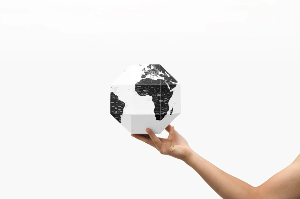 Ręka trzymająca globus z pinezkami w czarno-białym stylu marki WABOBA AB