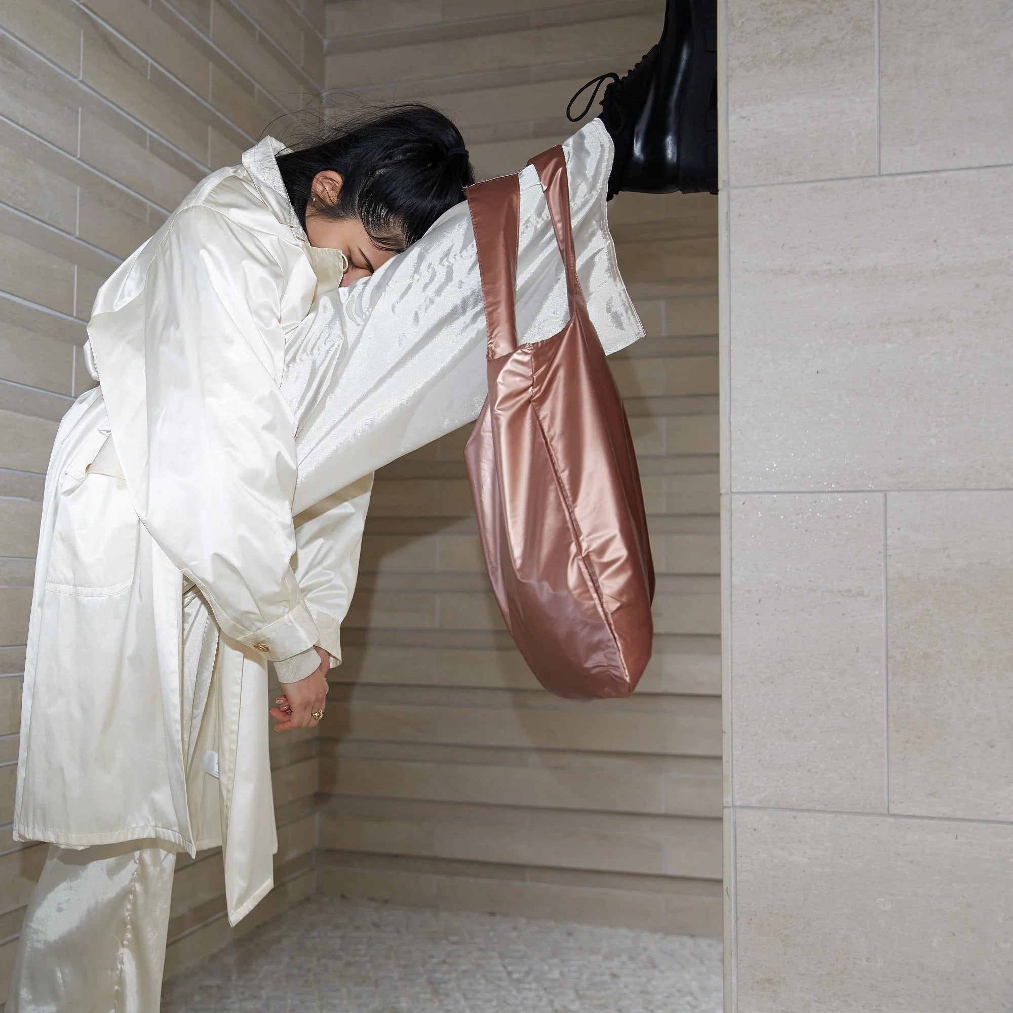 Torba LOQI metallic rose gold zawieszona na nodze kobiety ubranej w biały satynowy płaszcz