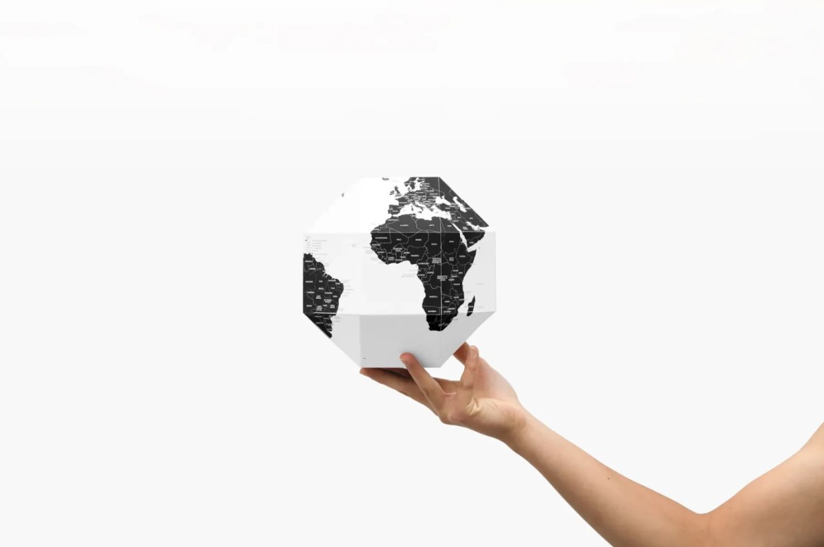 Ręka trzymająca minimalistyczny czarno-biały globus z pinezkami do oznaczania krajów firmy WABOBA AB