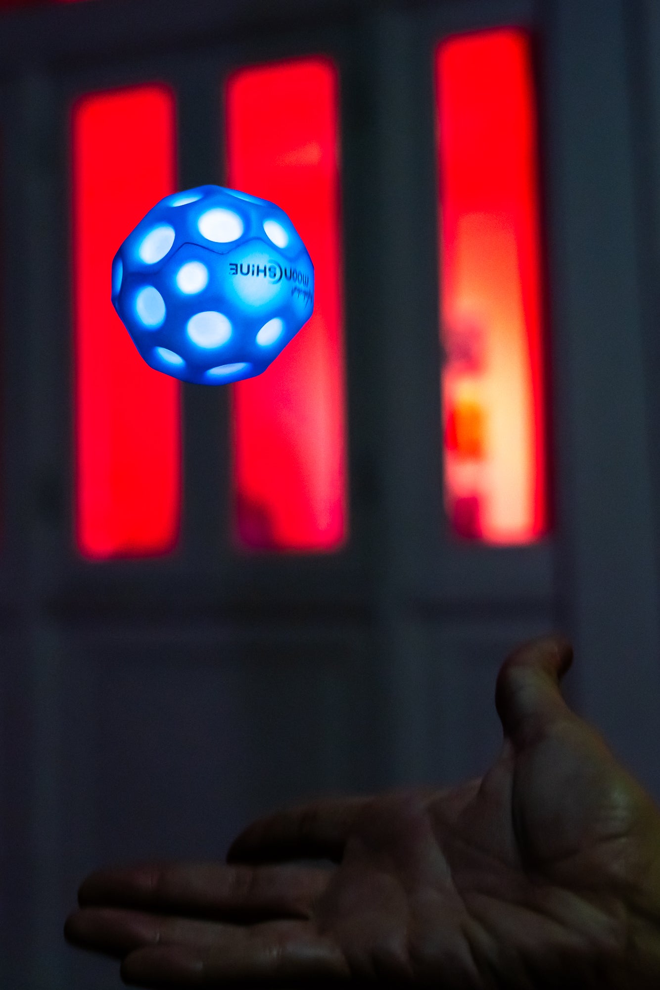 Ręka wyrzucająca niebieską piłeczkę Waboba Moonshine niebieską świecącą w ciemności