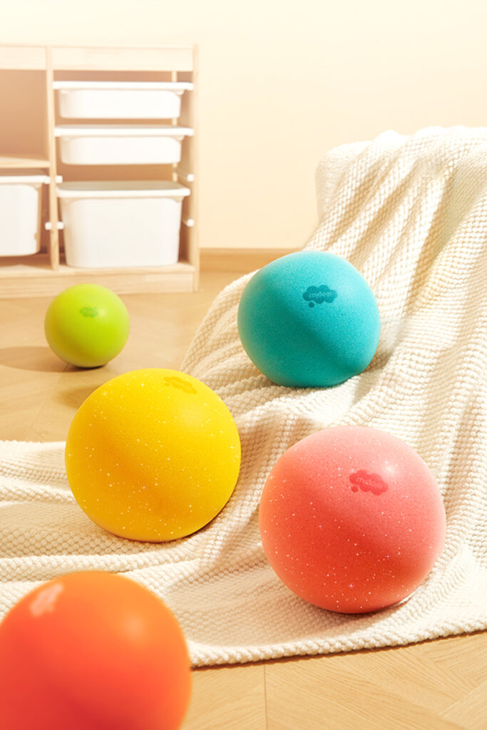 Kolorowe cicha piłka dla dzieci marki Yamann na drewnianej podłodze z kocem w tle