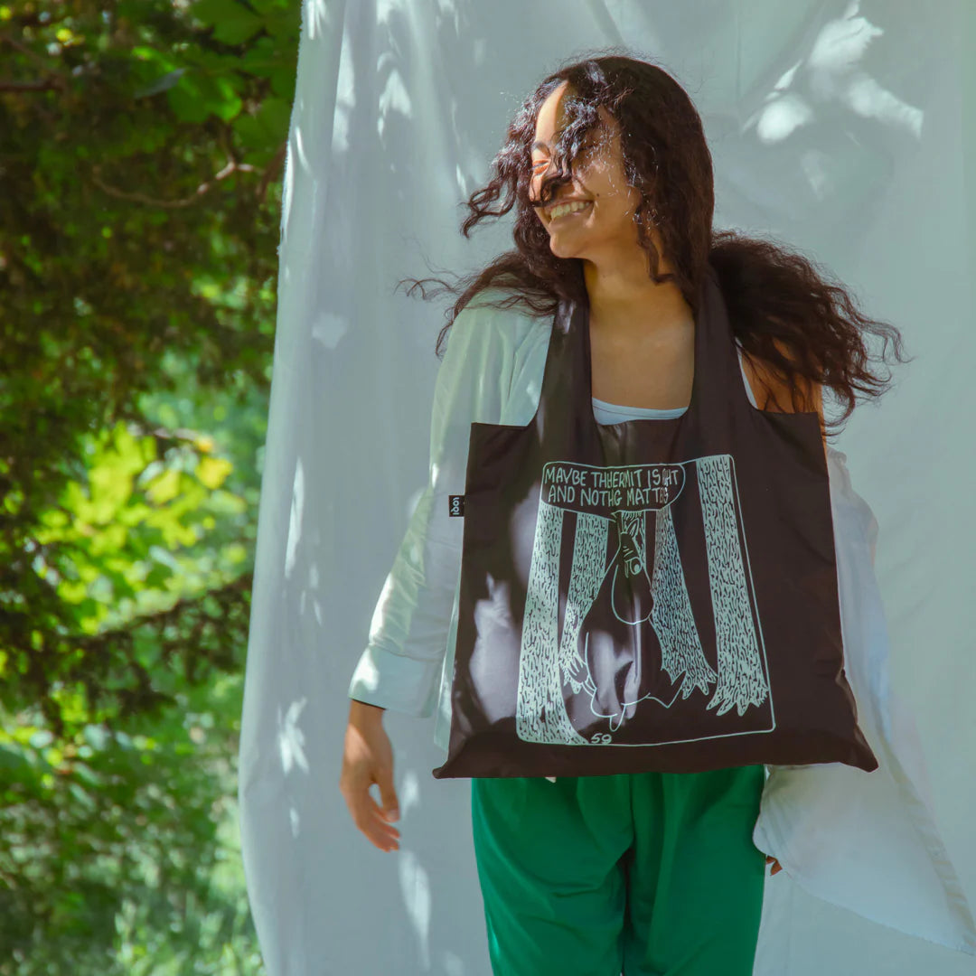 Kobieta nosząca czarną torbę LOQI Moomin z biało-czarnym nadrukiem Muminka w lesie