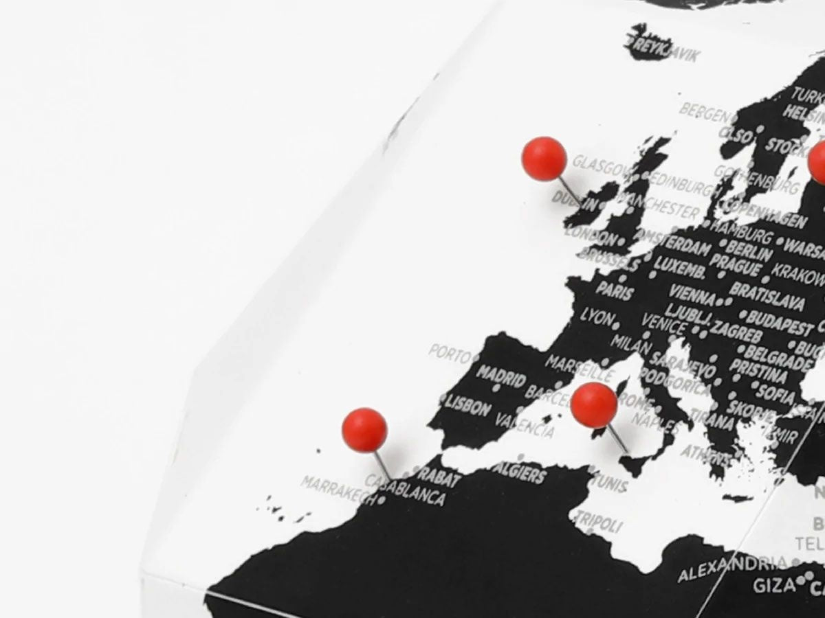 Czarnobiały globus z pinezkami pokazujący ważne miasta w Europie i Afryce