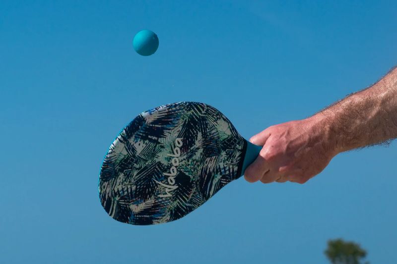 Paletki plażowe Waboba z piłką w ruchu na tle niebieskiego nieba podczas gry na plaży