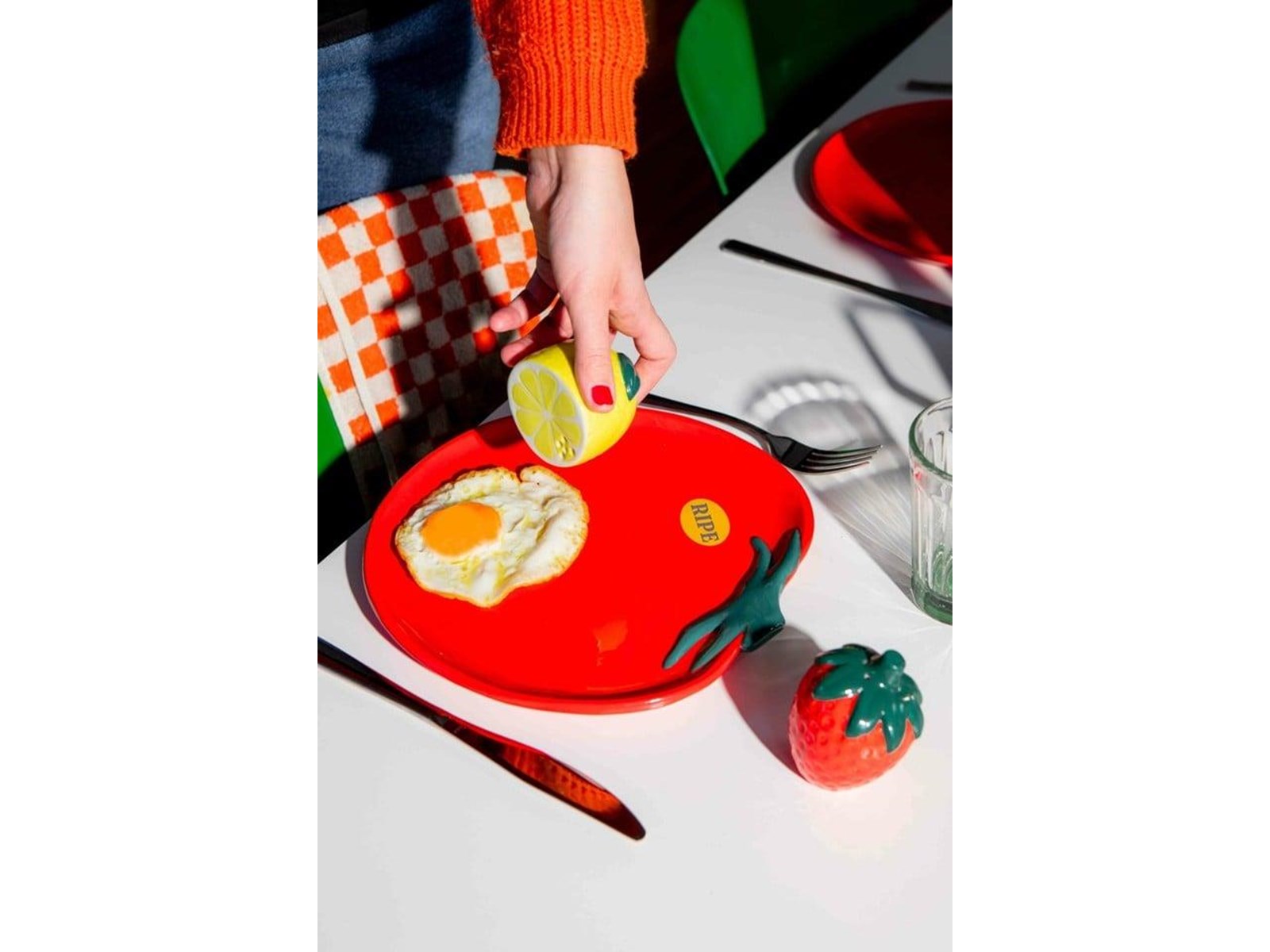 Solniczka i pieprzniczka truskawka cytryna marki DOIY na stole obok czerwonego talerza z jajkiem sadzonym