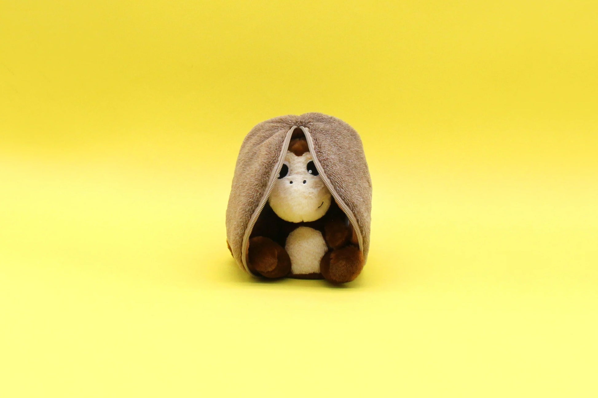 Maskotka małpa kokos siedząca owinięta brązowym kocem na żółtym tle