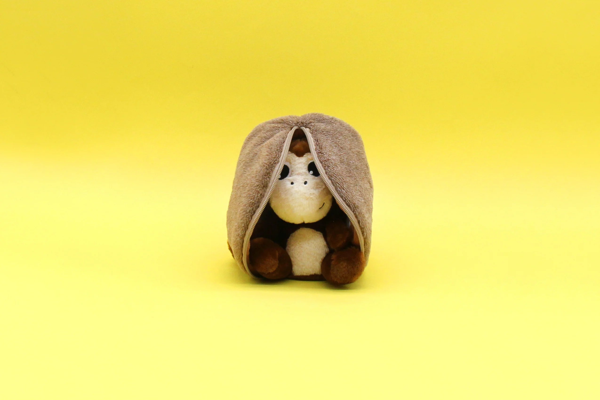 Maskotka małpa kokos siedząca owinięta brązowym kocem na żółtym tle