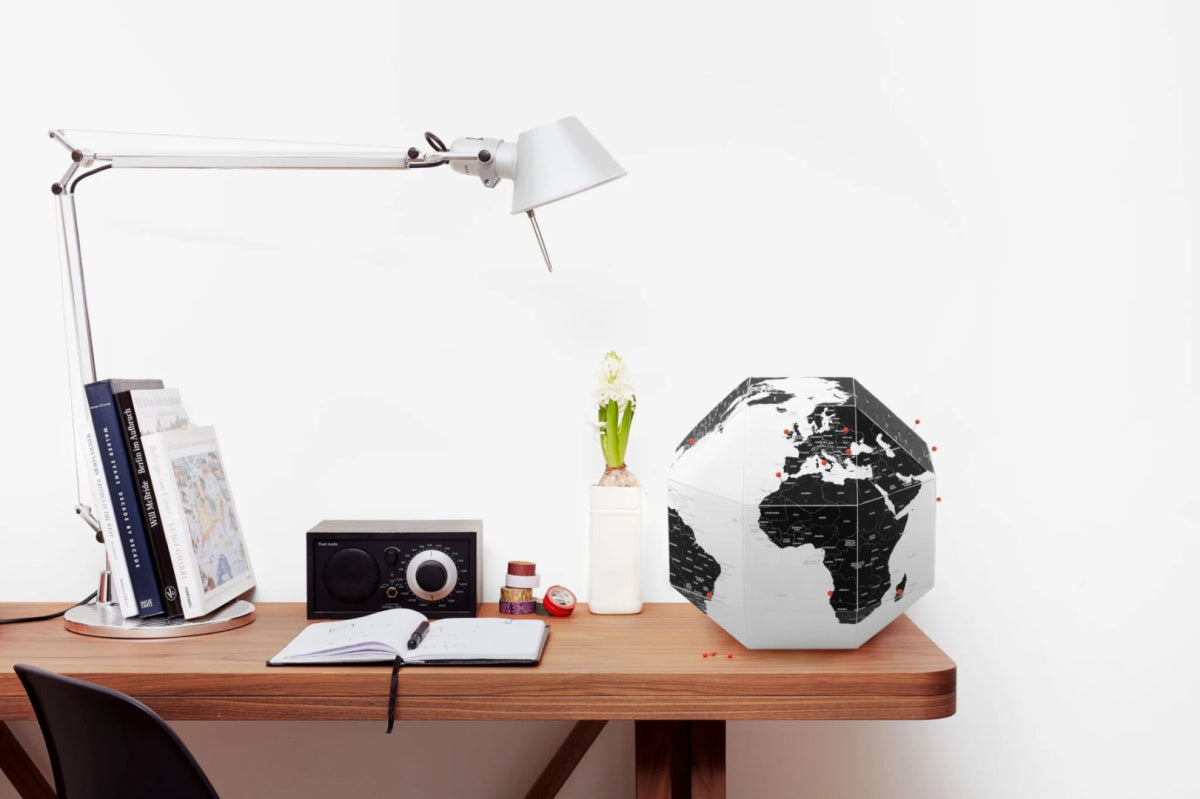 Nowoczesny globus z pinezkami na biurku obok lampy i książek do nauki geografii