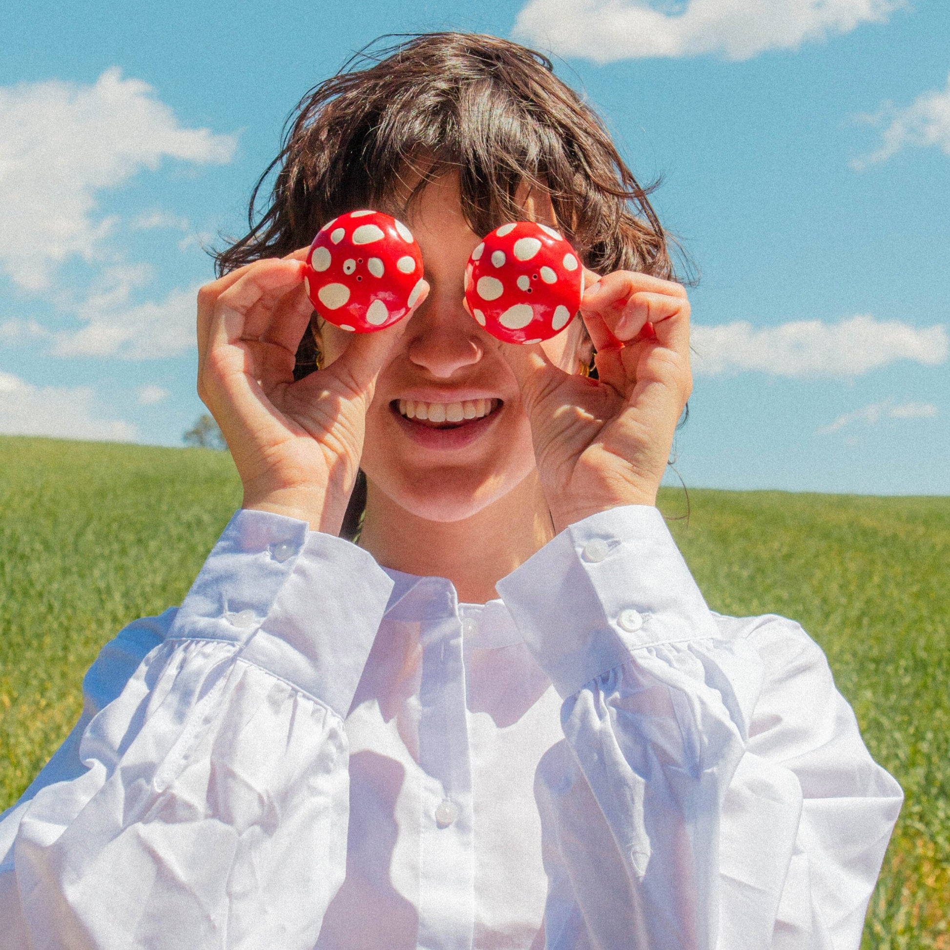 Solniczka i pieprzniczka muchomorki trzymane przez uśmiechniętą kobietę na tle zielonego pola i nieba