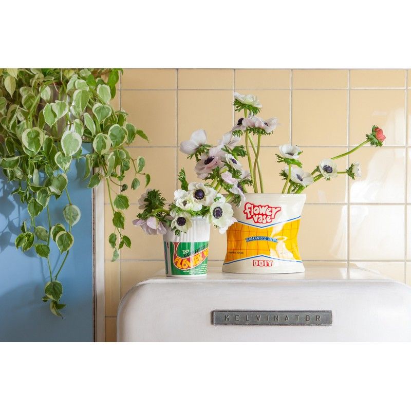 Wazon dekoracyjny paczka chipsów z kwiatami stojący na białej lodówce obok zielonej rośliny