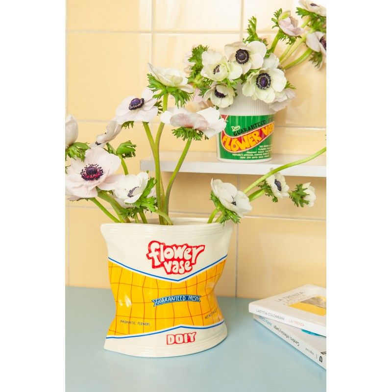 wazon dekoracyjny paczka chipsów z kwiatami na niebieskim blacie i książkami obok