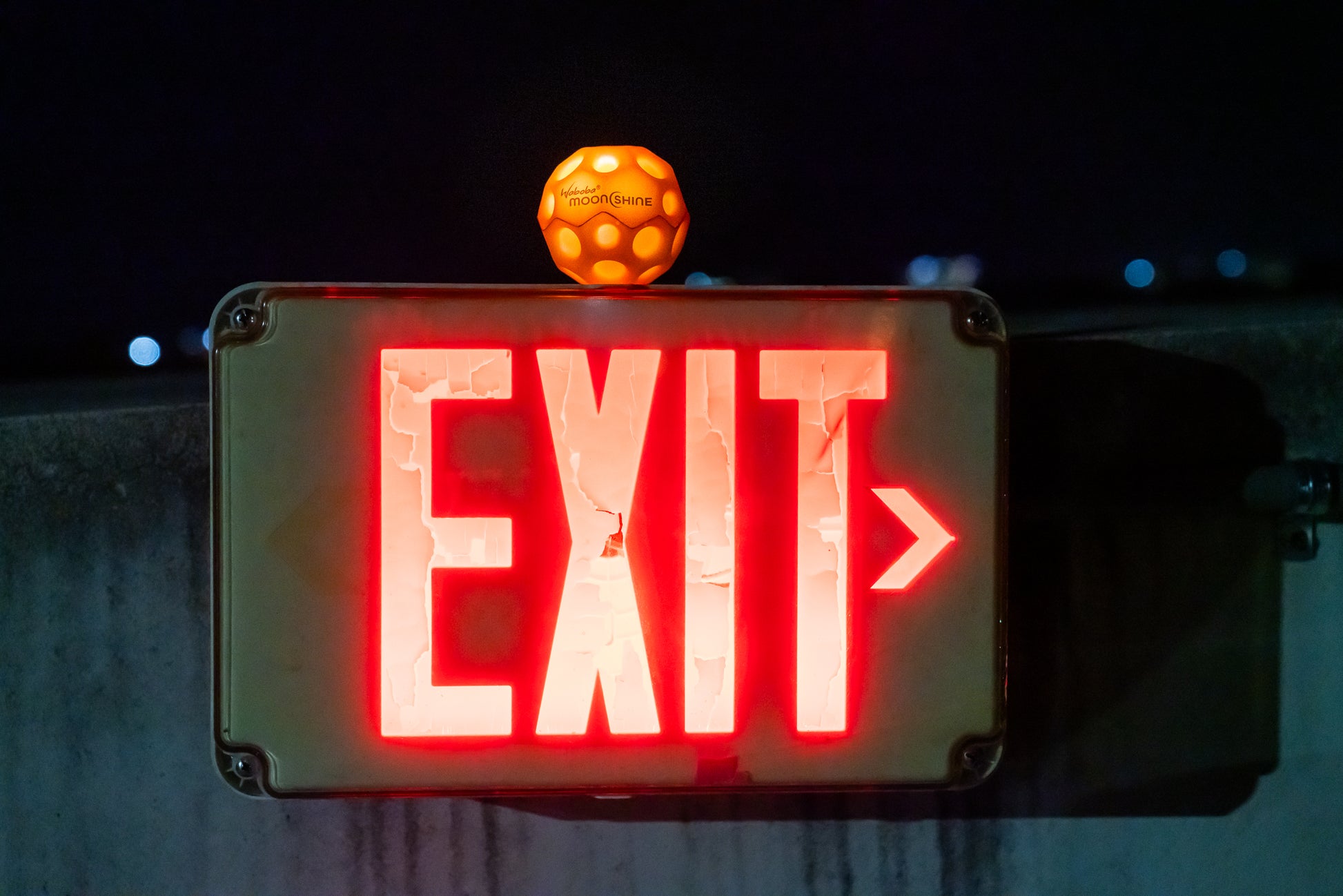 Pomarańczowa piłeczka świecąca Waboba Moonshine na znaku wyjścia awaryjnego z czerwonym podświetleniem