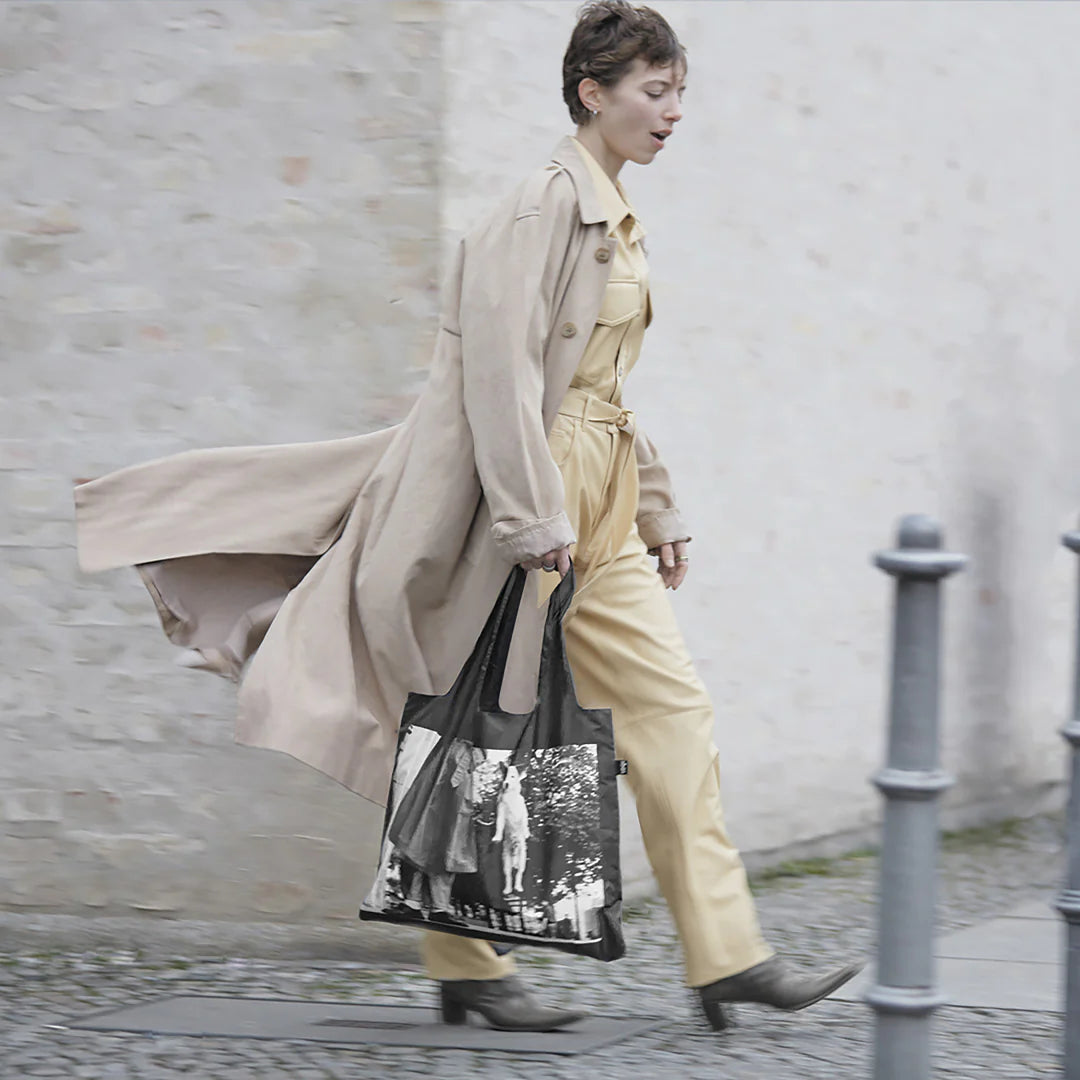 Kobieta idąca z beżowym płaszczem trzymająca torbę LOQI z psem w czarno-białym wzorze