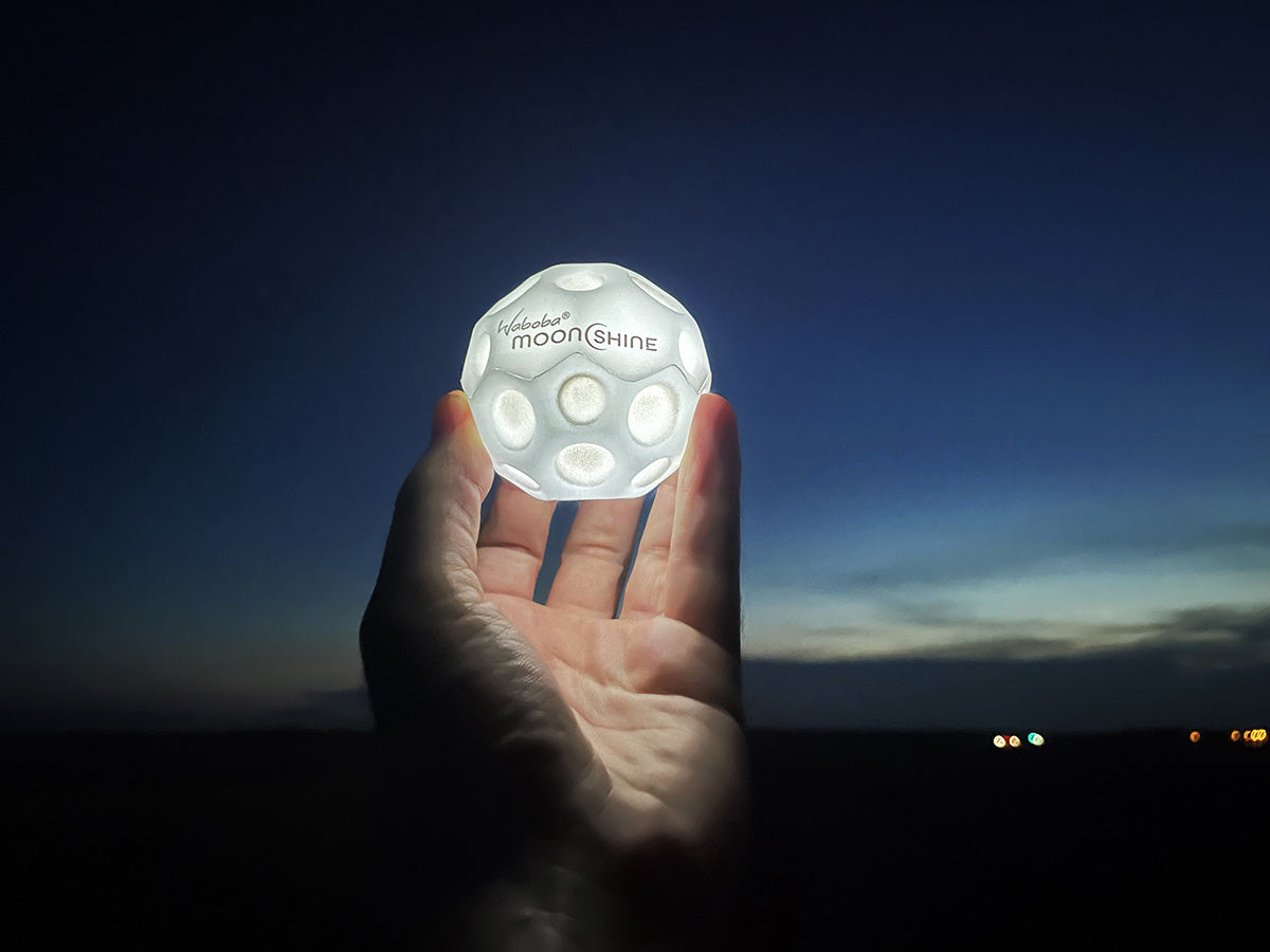 Ręka trzymająca świecącą w ciemności piłeczkę Waboba Moonshine na tle nocnego nieba